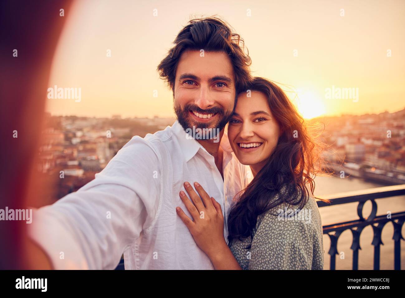 Feliz pareja amorosa tomando selfie a través de teléfono inteligente en frente de la ciudad de Oporto al atardecer, Portugal Foto de stock