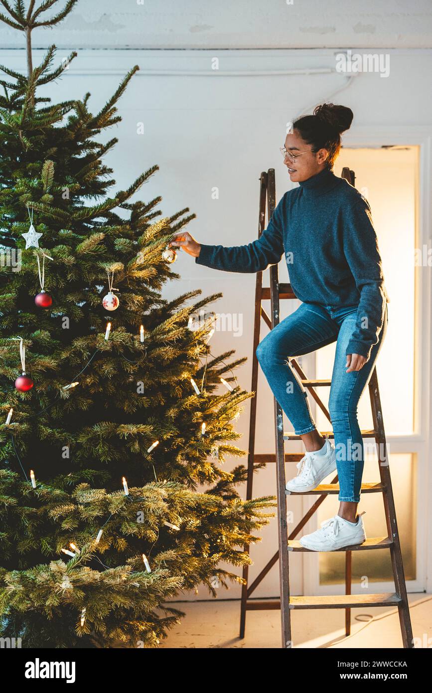 Mujer joven que decora el árbol de Navidad que se coloca en la escalera Foto de stock