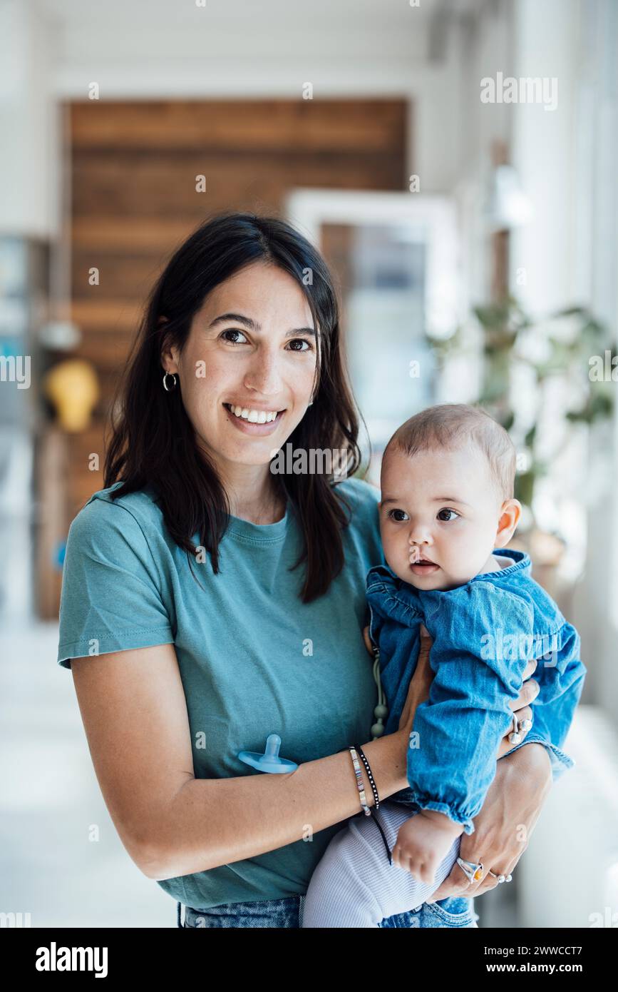 Madre feliz que lleva a la niña en la sala de estar en casa Foto de stock