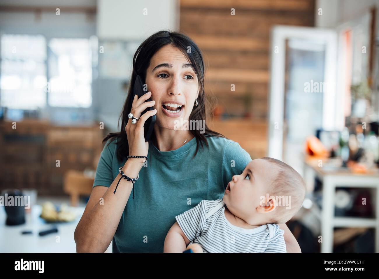 Bebé curioso mirando a la madre hablando en el teléfono móvil Foto de stock