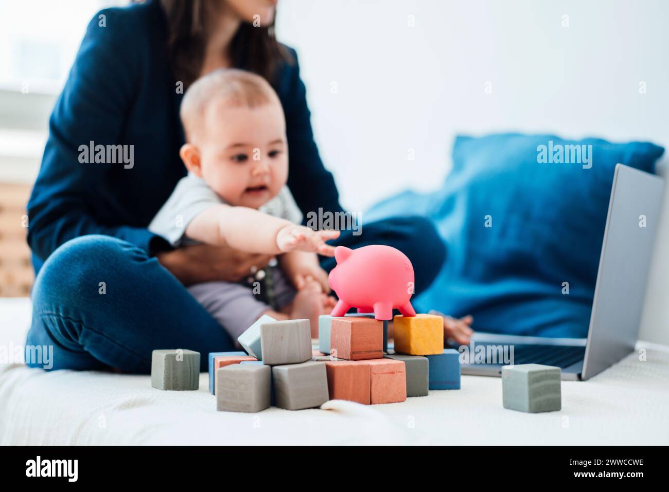 Bebé niña que llega al banco piggy sentado en empresaria usando el ordenador portátil en la cama Foto de stock