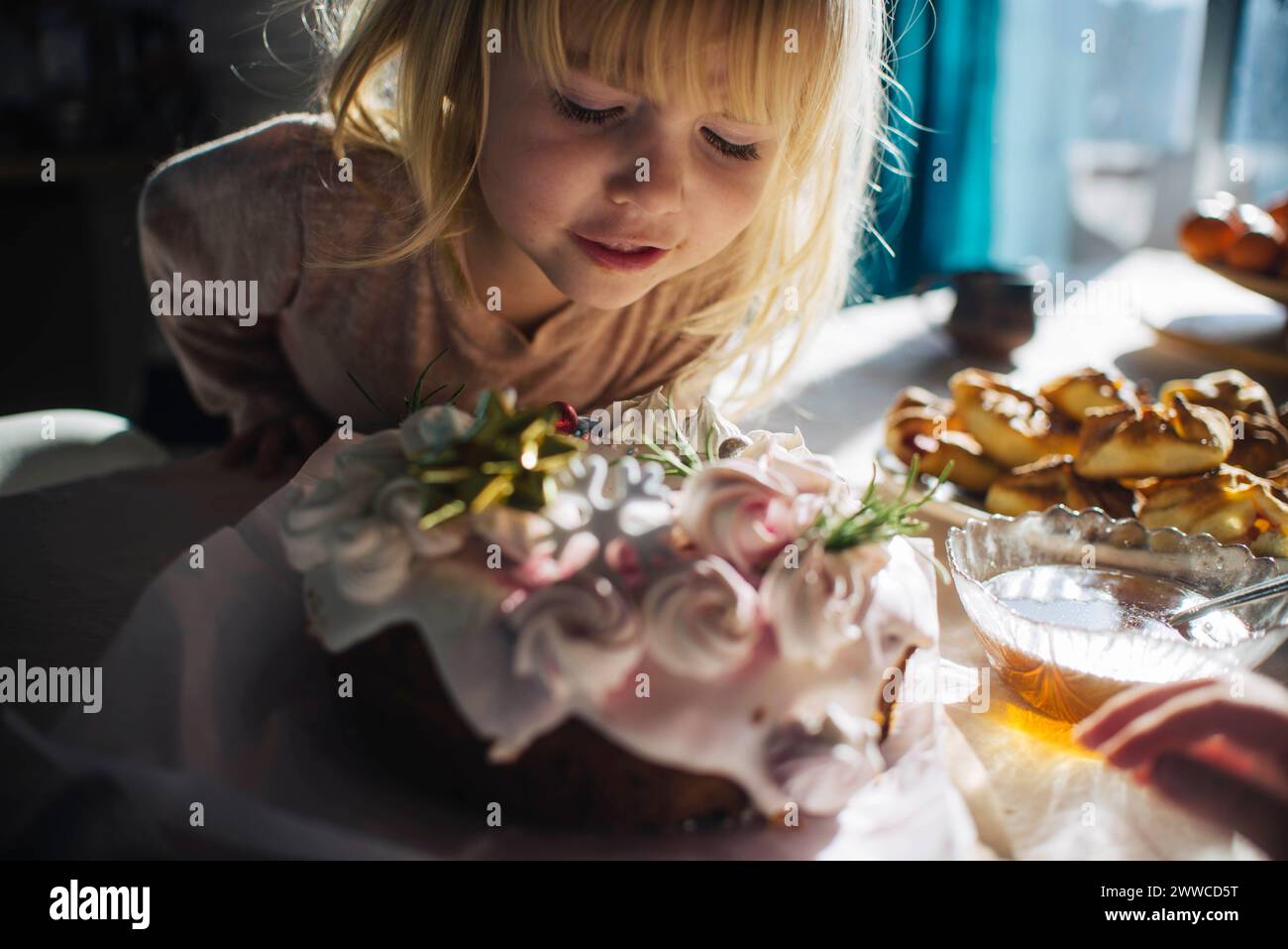 Chica curiosa mirando pastel de cumpleaños en la mesa Foto de stock