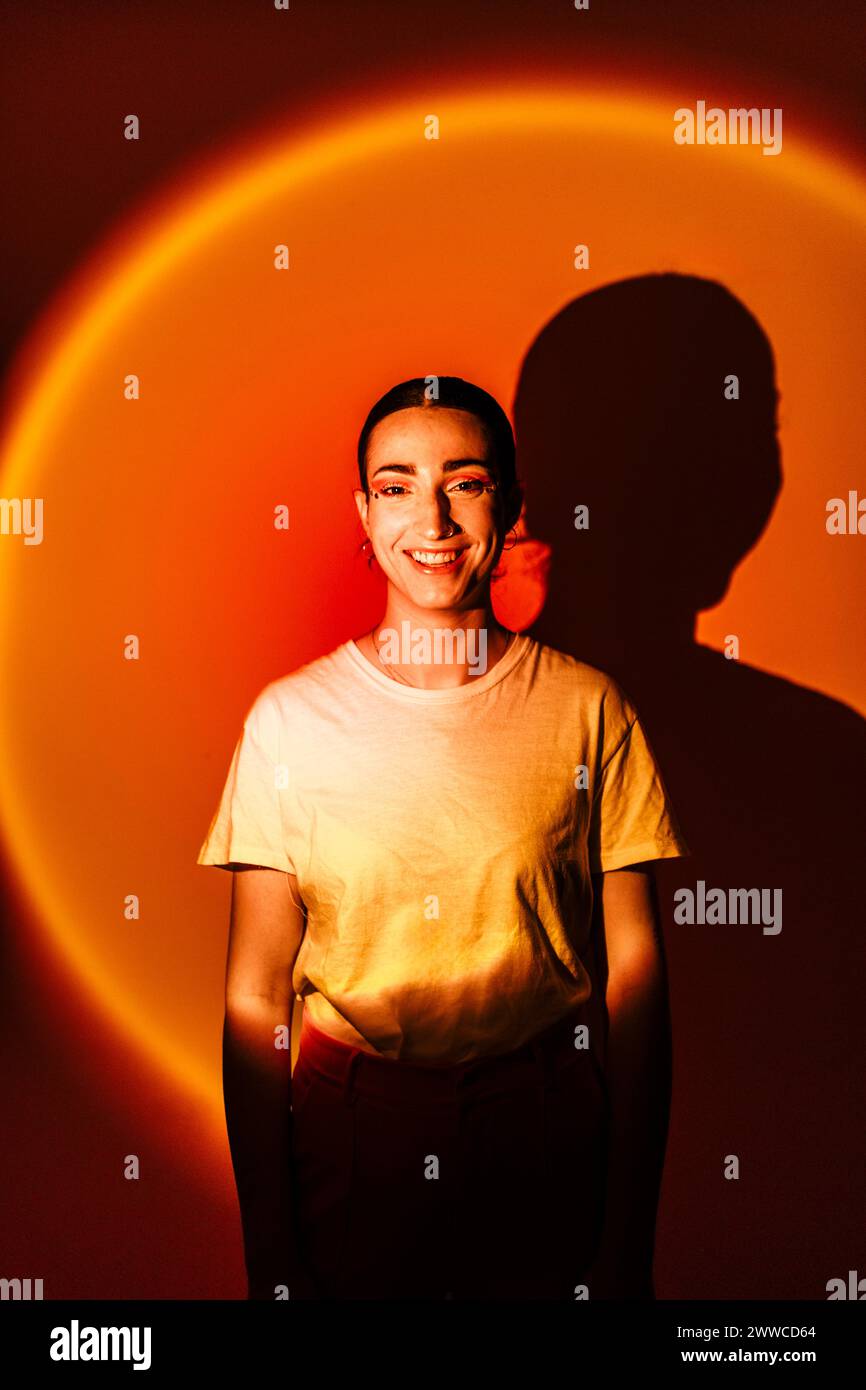 Mujer joven feliz de pie en la iluminación de neón contra el fondo naranja Foto de stock