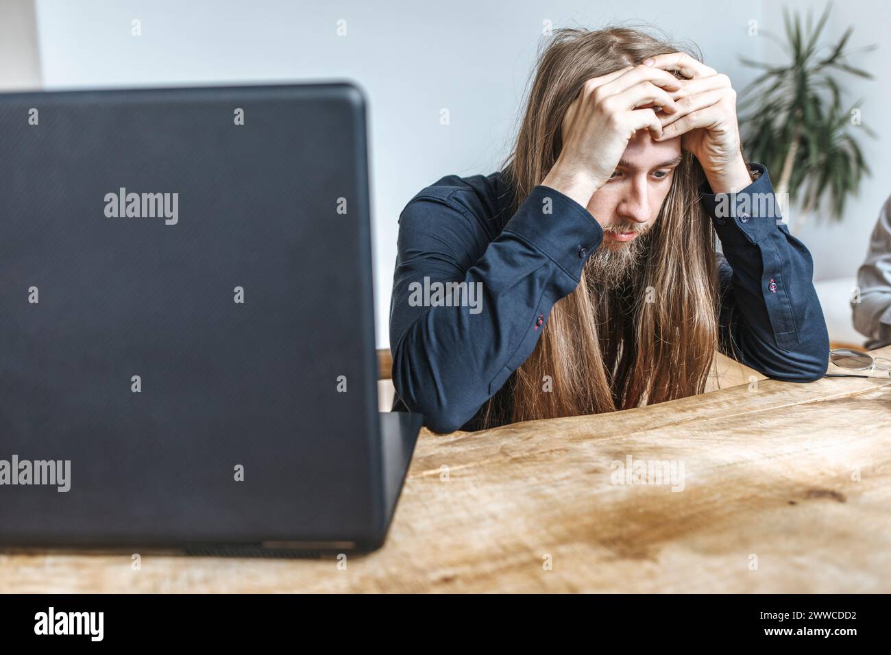 Programador hipster estresado sentado con la cabeza en las manos por el ordenador portátil en la mesa en la oficina Foto de stock