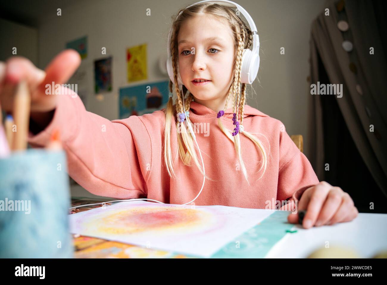 Muchacha que lleva auriculares que toman el lápiz del organizador del escritorio en la mesa Foto de stock