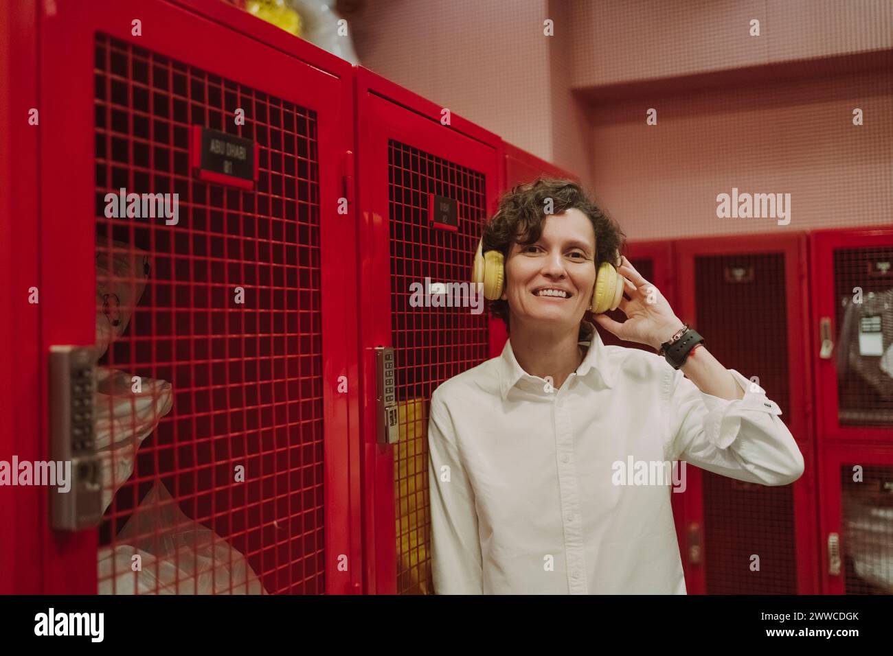 Mujer feliz que lleva auriculares inalámbricos que escuchan la música apoyada en el armario rojo Foto de stock