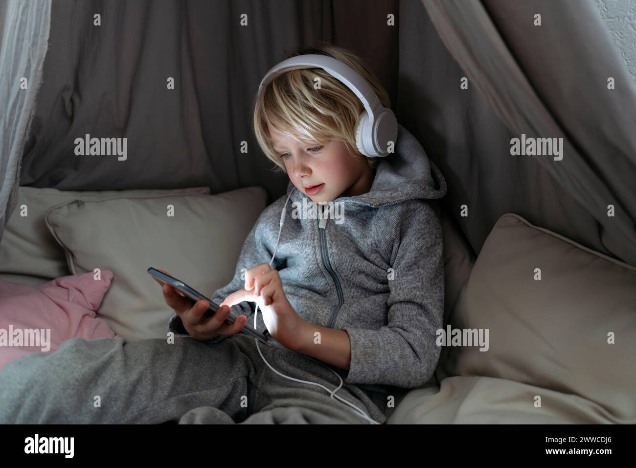 Muchacho que lleva auriculares usando Internet en el teléfono inteligente en el dosel en casa Foto de stock