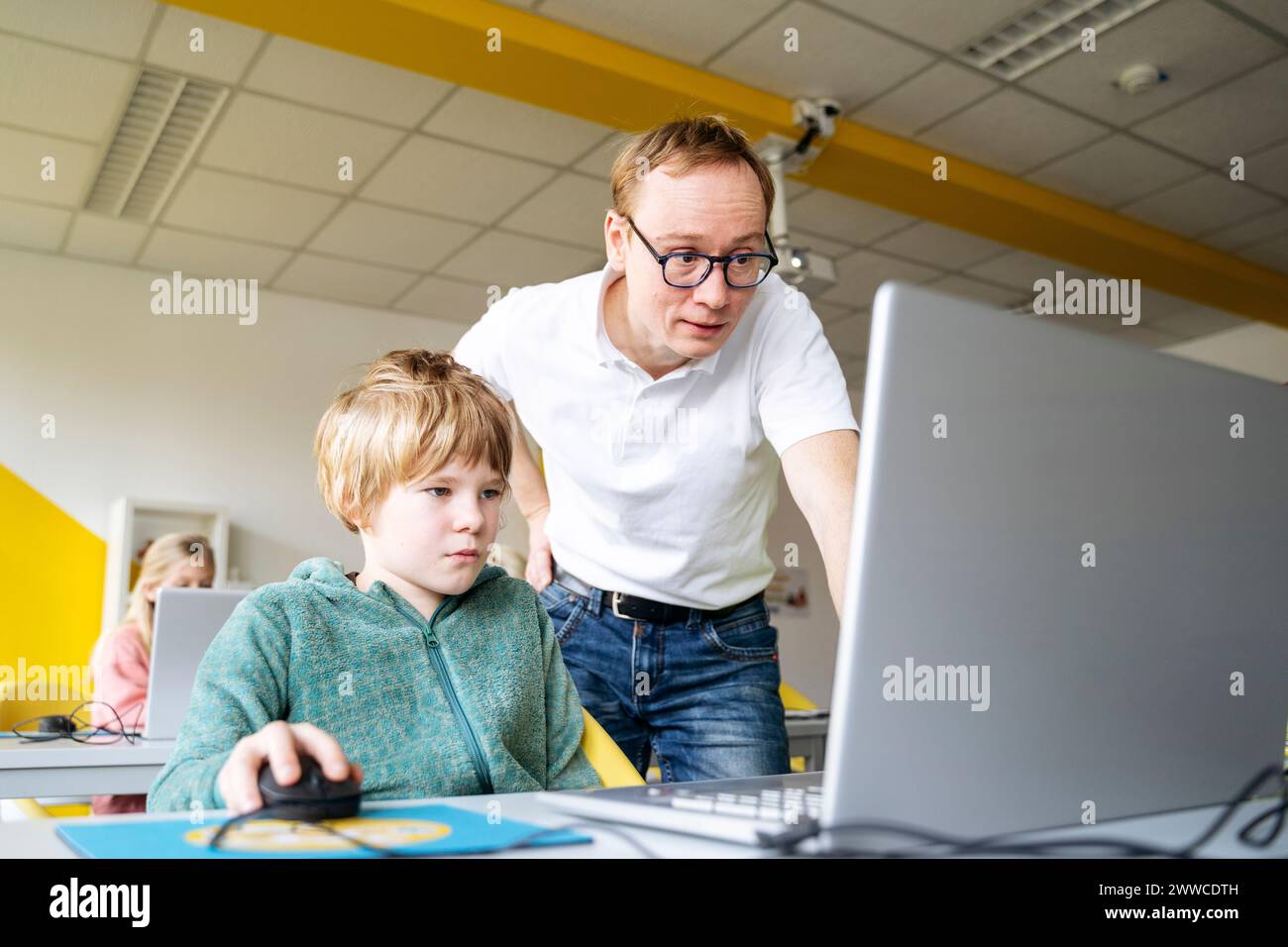 Profesor que ayuda al niño con la codificación en el ordenador portátil en el escritorio Foto de stock