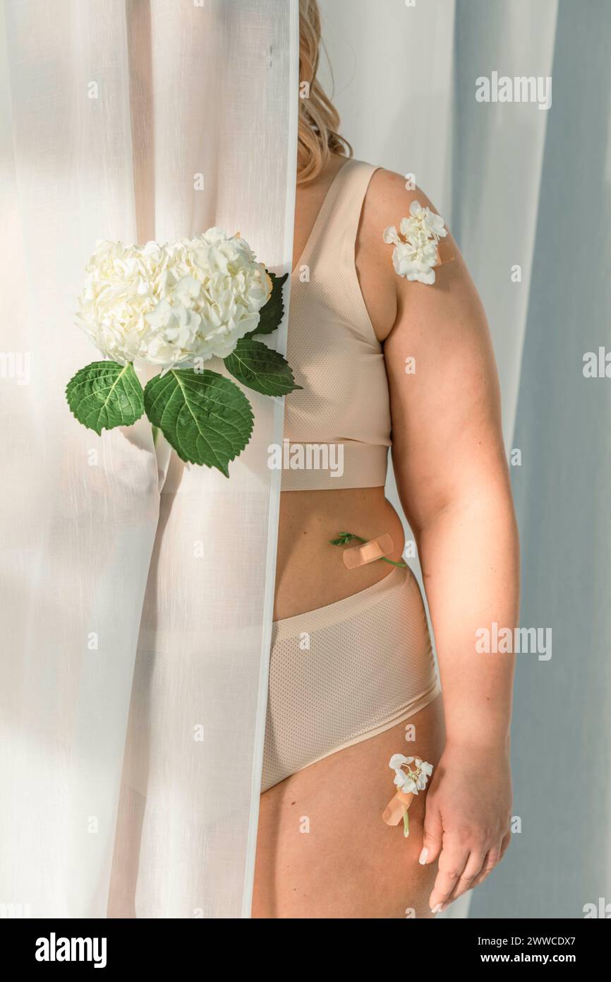Mujer con flores en el cuerpo que se esconde detrás de la cortina blanca Foto de stock
