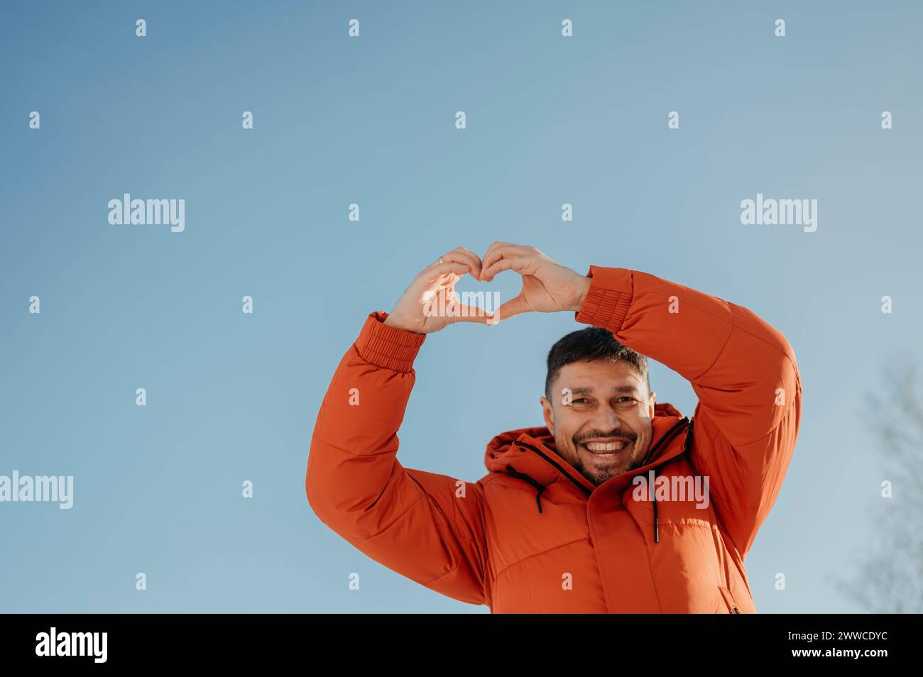 Hombre sonriente que muestra hacer gesto de forma de corazón con el cielo en el fondo Foto de stock