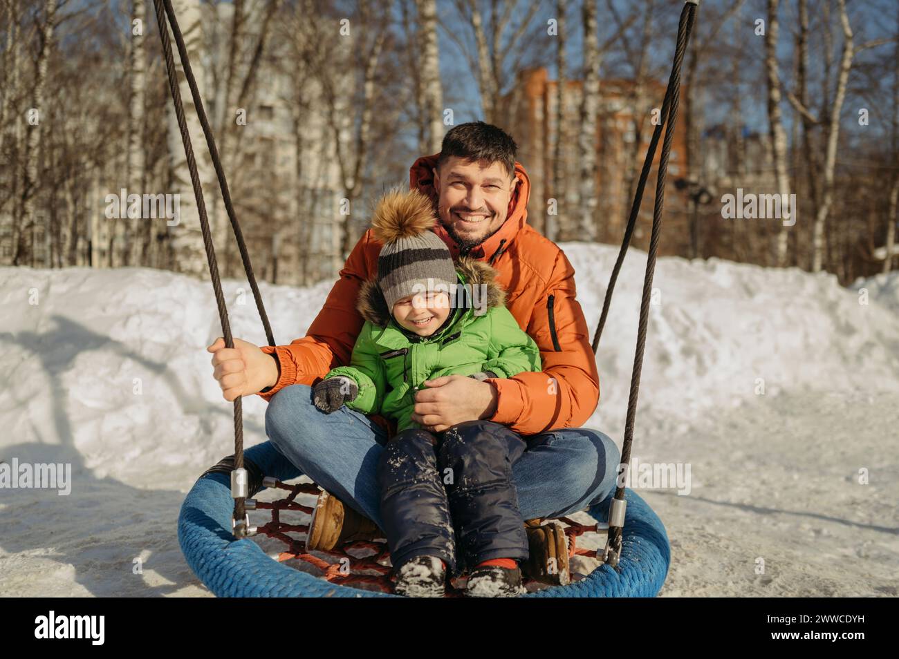 Hombre sonriente balanceándose con el hijo en el parque en invierno Foto de stock