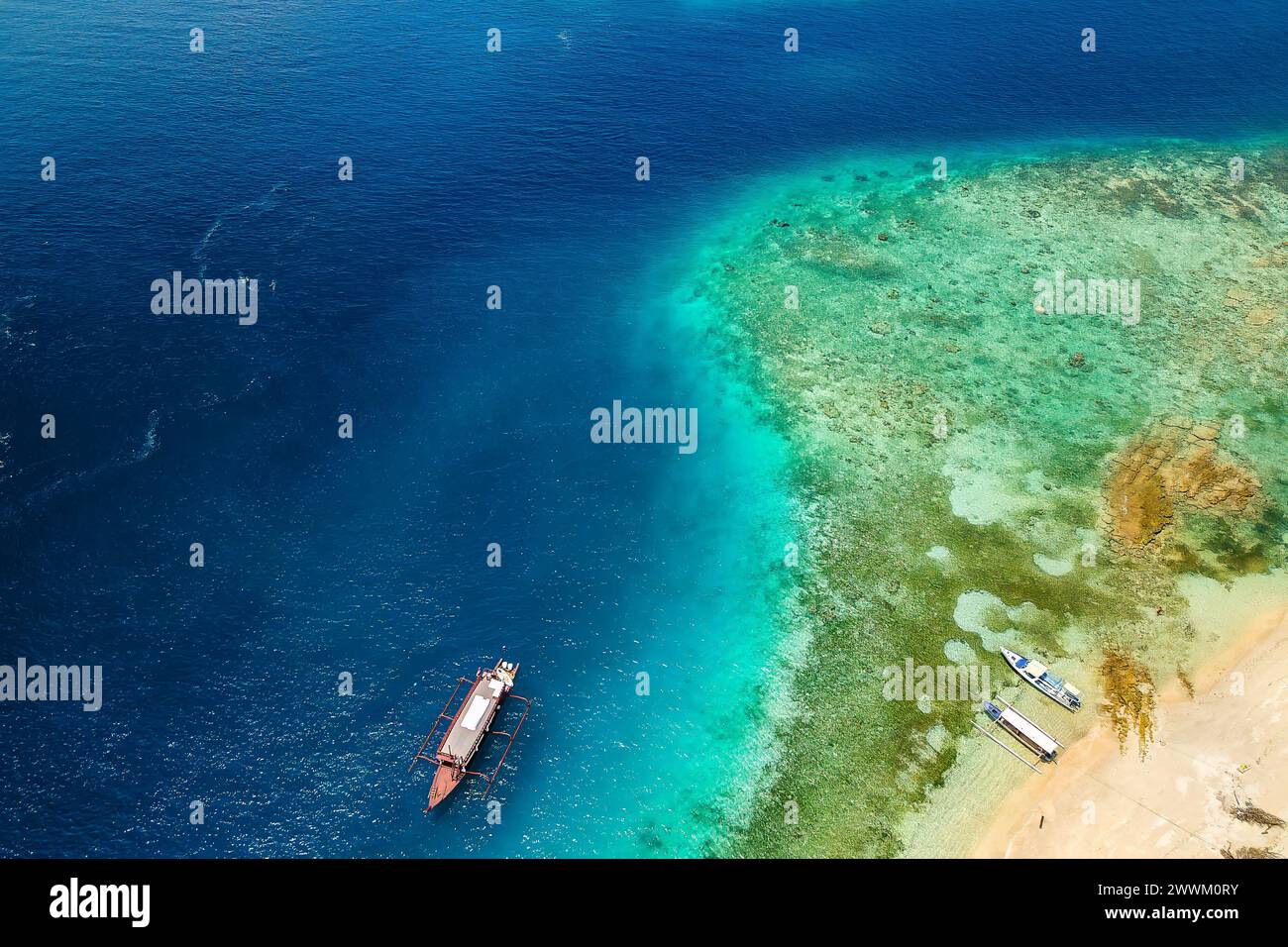 Barcos turísticos amarrados en el borde de un arrecife de coral bordeado de la costa de una isla tropical durante una marea baja Foto de stock