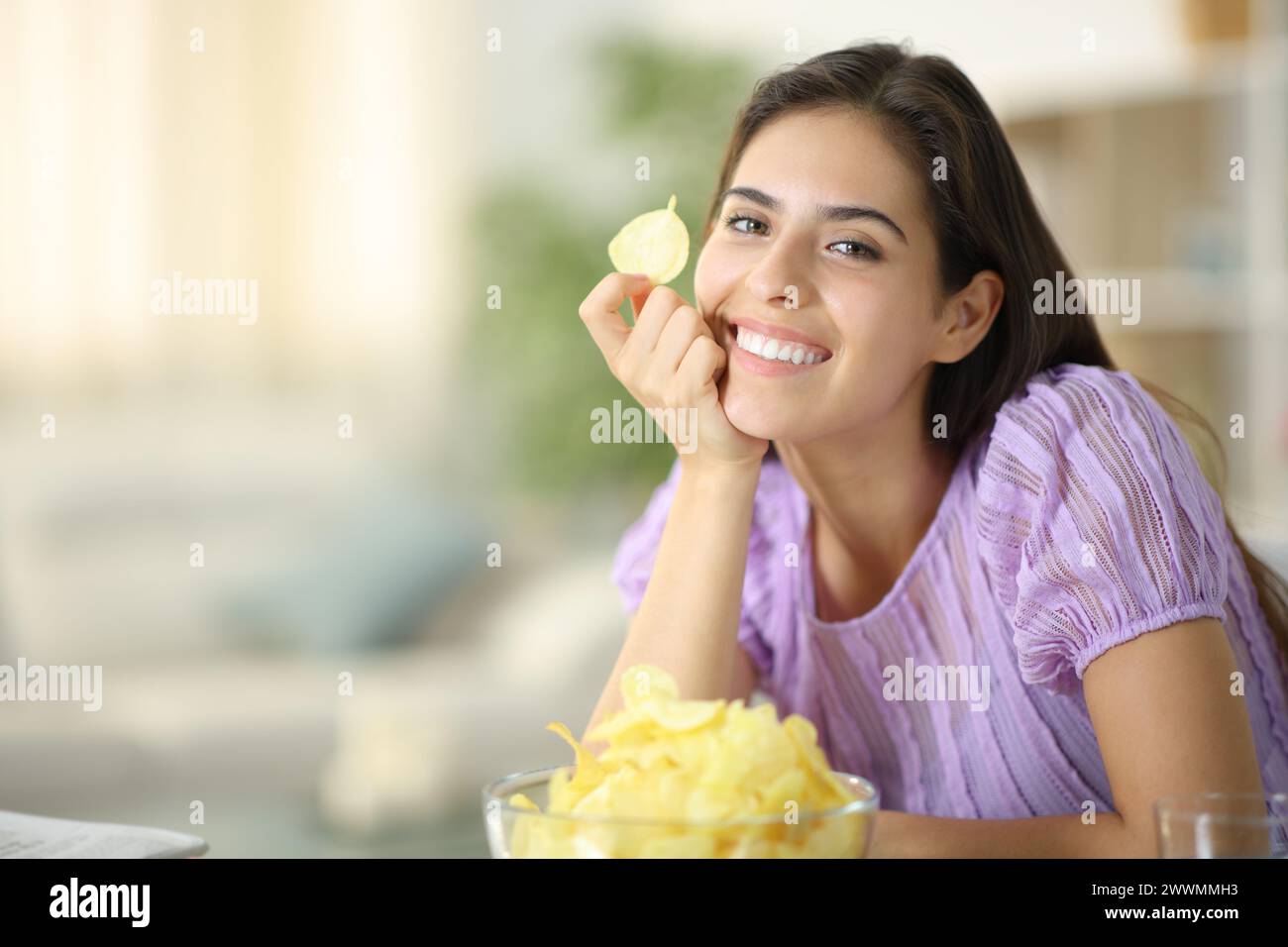 Mujer feliz posando sosteniendo chip de patata mirando a la cámara en casa Foto de stock
