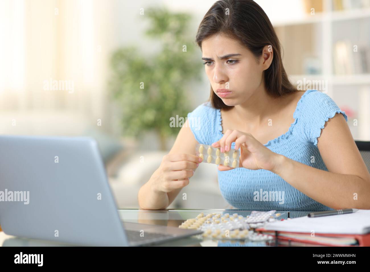 Estudiante estresado tomando pastillas estudiando en línea con una computadora portátil en casa Foto de stock