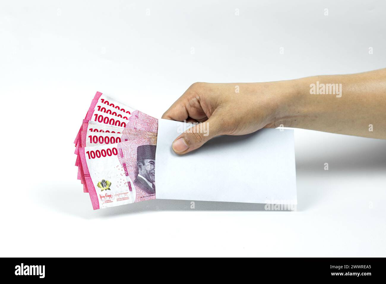 Mano del hombre asiático sosteniendo sobre blanco que contiene la pila de IDR 100.000 efectivo. Moneda de la rupia indonesia Foto de stock
