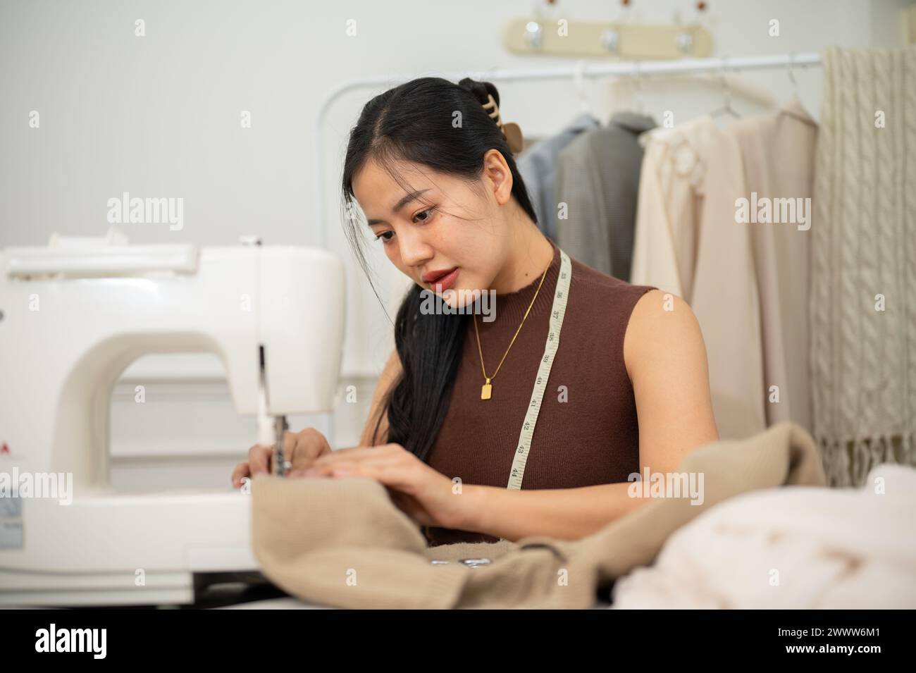 Una sastre asiática profesional o diseñadora de moda está cosiendo un vestido con una máquina de coser, trabajando en su nueva colección de ropa en su estudio. Foto de stock