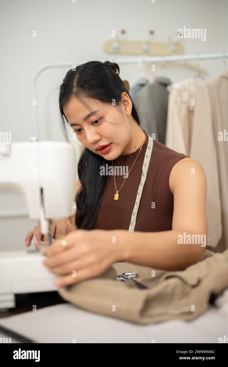 Una sastre asiática profesional o diseñadora de moda está cosiendo un vestido con una máquina de coser, trabajando en su nueva colección de ropa en su estudio. Foto de stock