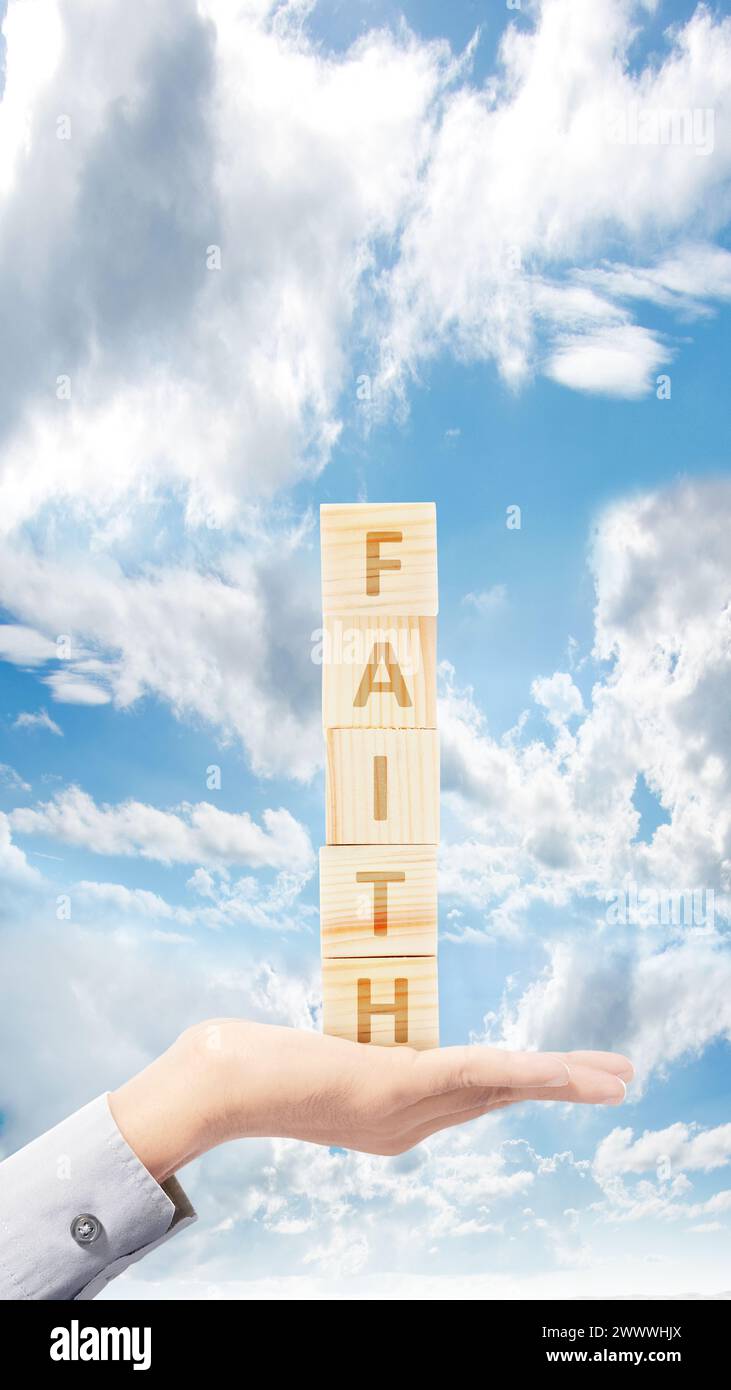 Una mano humana sosteniendo una pila de un cubo con el texto de la fe con un fondo de cielo azul. Concepto cristiano Foto de stock