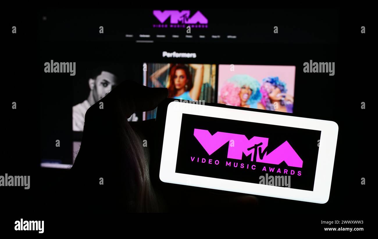 Persona que sostiene el teléfono móvil con el logotipo del programa de premios MTV Video Music Awards (VMA) frente a la página web de la compañía. Enfoque en la pantalla del teléfono. Foto de stock