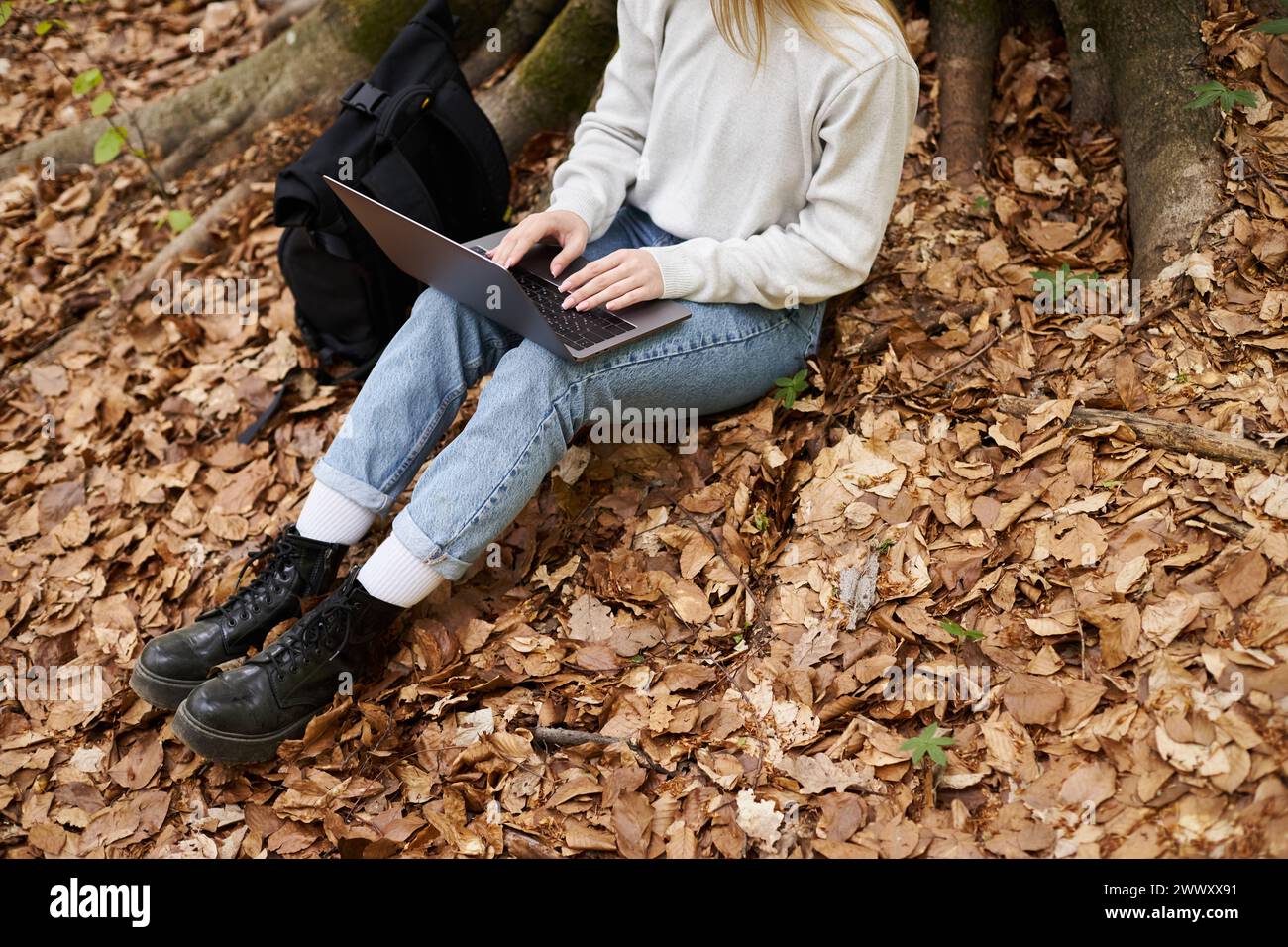 Vista recortada de la mujer caminante con el ordenador portátil en sus rodillas trabajando a distancia mientras se sienta en el bosque en viaje Foto de stock