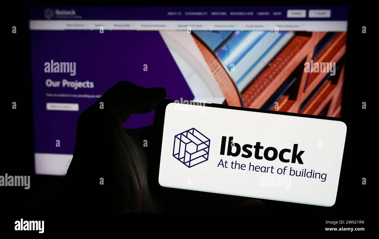 Persona que sostiene el teléfono móvil con el logotipo de la empresa británica de materiales de construcción Ibstock plc frente a la página web del negocio. Enfoque en la pantalla del teléfono. Foto de stock