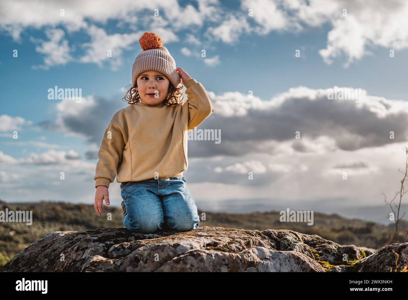 niño de moda con el sombrero jugando y feliz, preguntándose, en la cima de una roca, en un castillo de piedra con vista panorámica de las montañas, en el día soleado a Foto de stock