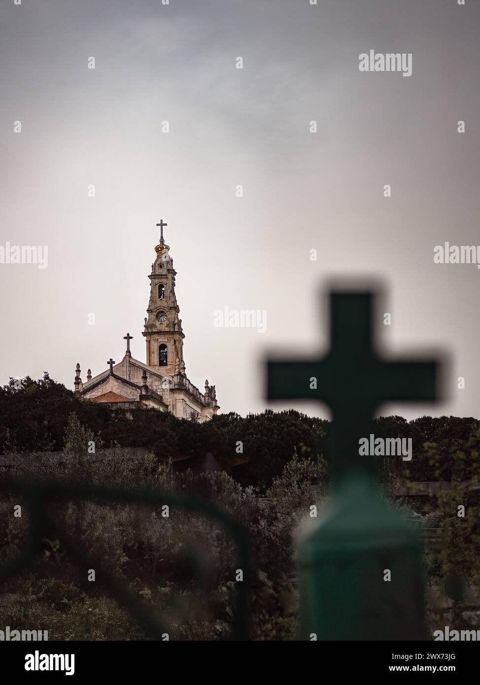 Fátima, PORTUGAL - 23 de marzo de 2024: Composición con la Basílica de Nuestra Señora del Rosario en el Santuario de Fátima enmarcada por una cruz cristiana borrosa Foto de stock