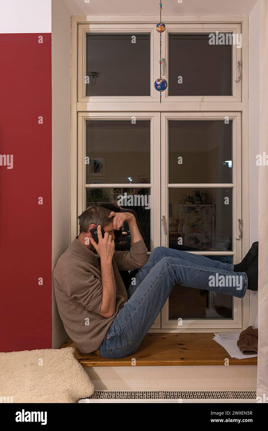 Joven sentado en la ventana mientras habla por teléfono, Mecklemburgo-Pomerania, Alemania Foto de stock