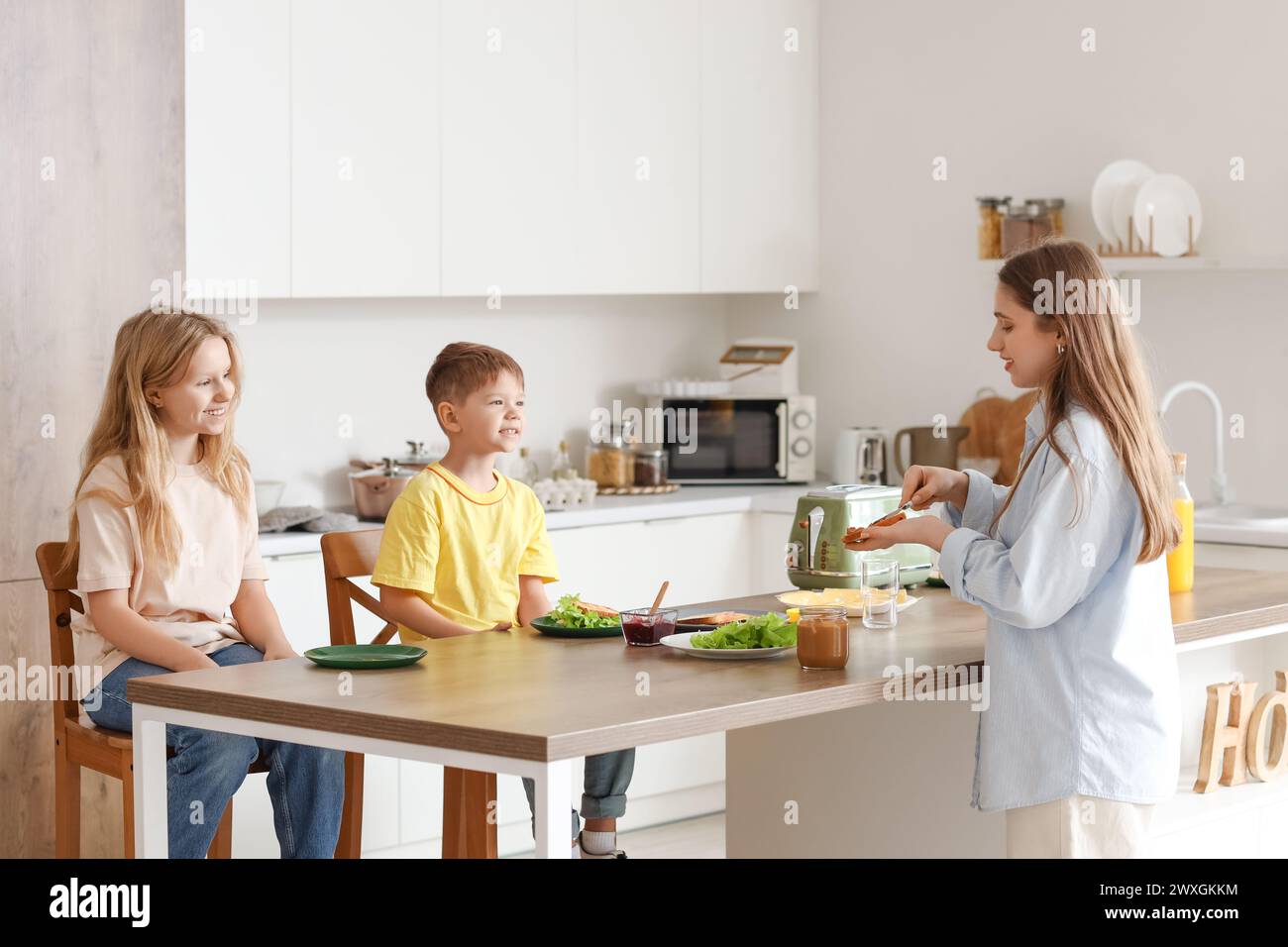 Madre con sus hijos pequeños haciendo tostadas en la cocina Foto de stock