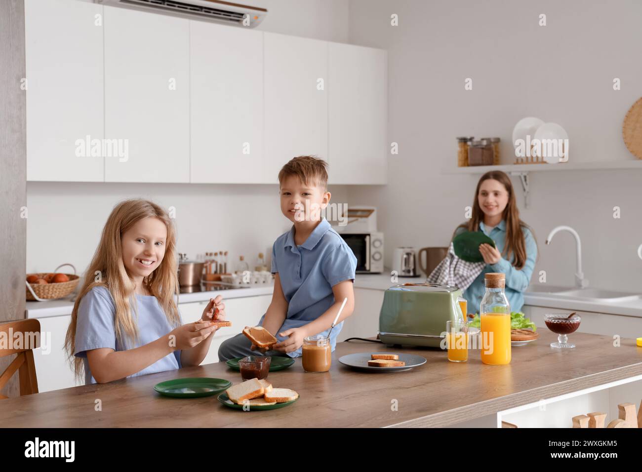 Niños pequeños con su madre haciendo tostadas en la cocina Foto de stock