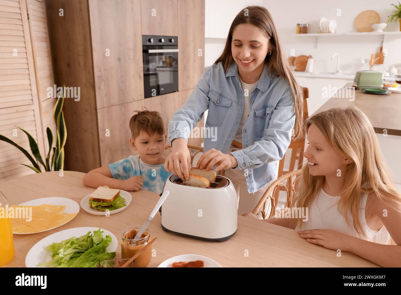 Niños pequeños con su madre haciendo tostadas en la mesa en la cocina Foto de stock