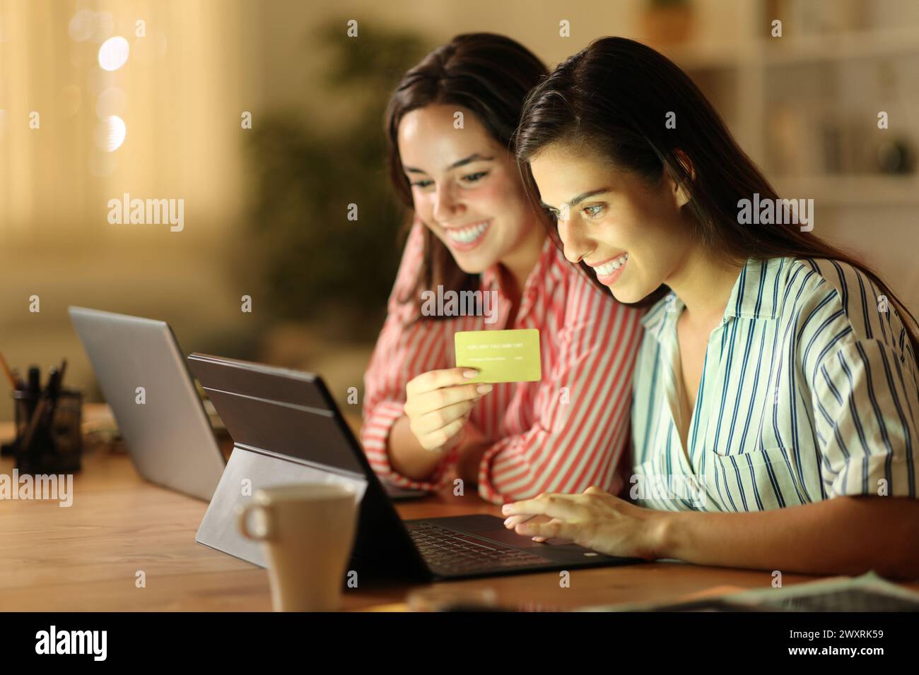 Dos teletrabajadores que compran en línea con tableta y tarjeta de crédito en casa en la noche Foto de stock