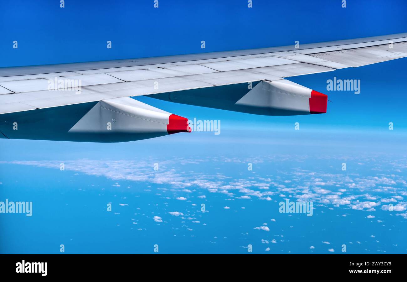 Ala de avión con pilones rojos en vuelo con capa superior de nubes blancas hinchadas Foto de stock