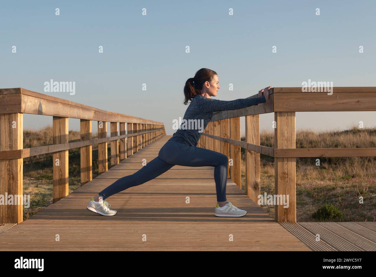 FIT mujer deportiva haciendo ejercicios de estiramiento en un paseo marítimo de madera Foto de stock