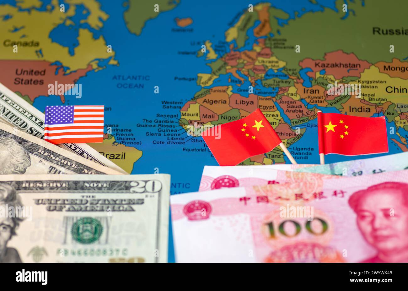 Un concepto de economía geopolítica con dólares estadounidenses, bandera estadounidense, yuan chino y banderas en la parte superior de un mapa del mundo. Foto de stock