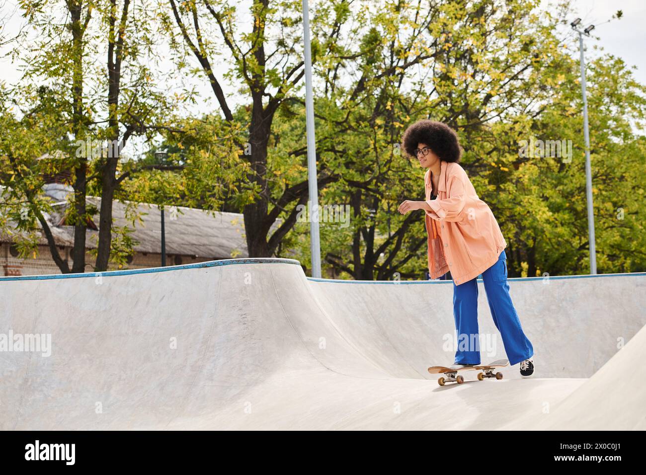 Una joven mujer afroamericana con el pelo rizado montando hábilmente un monopatín en un vibrante parque de skate. Foto de stock
