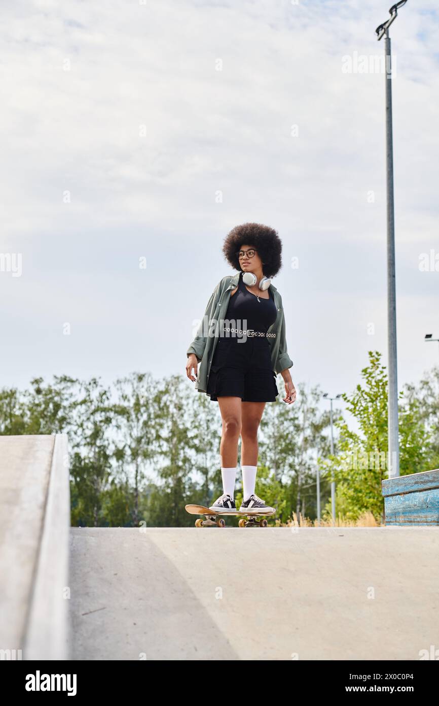 Una joven afroamericana con patinaje de pelo rizado por una rampa en un parque de patinaje. Foto de stock