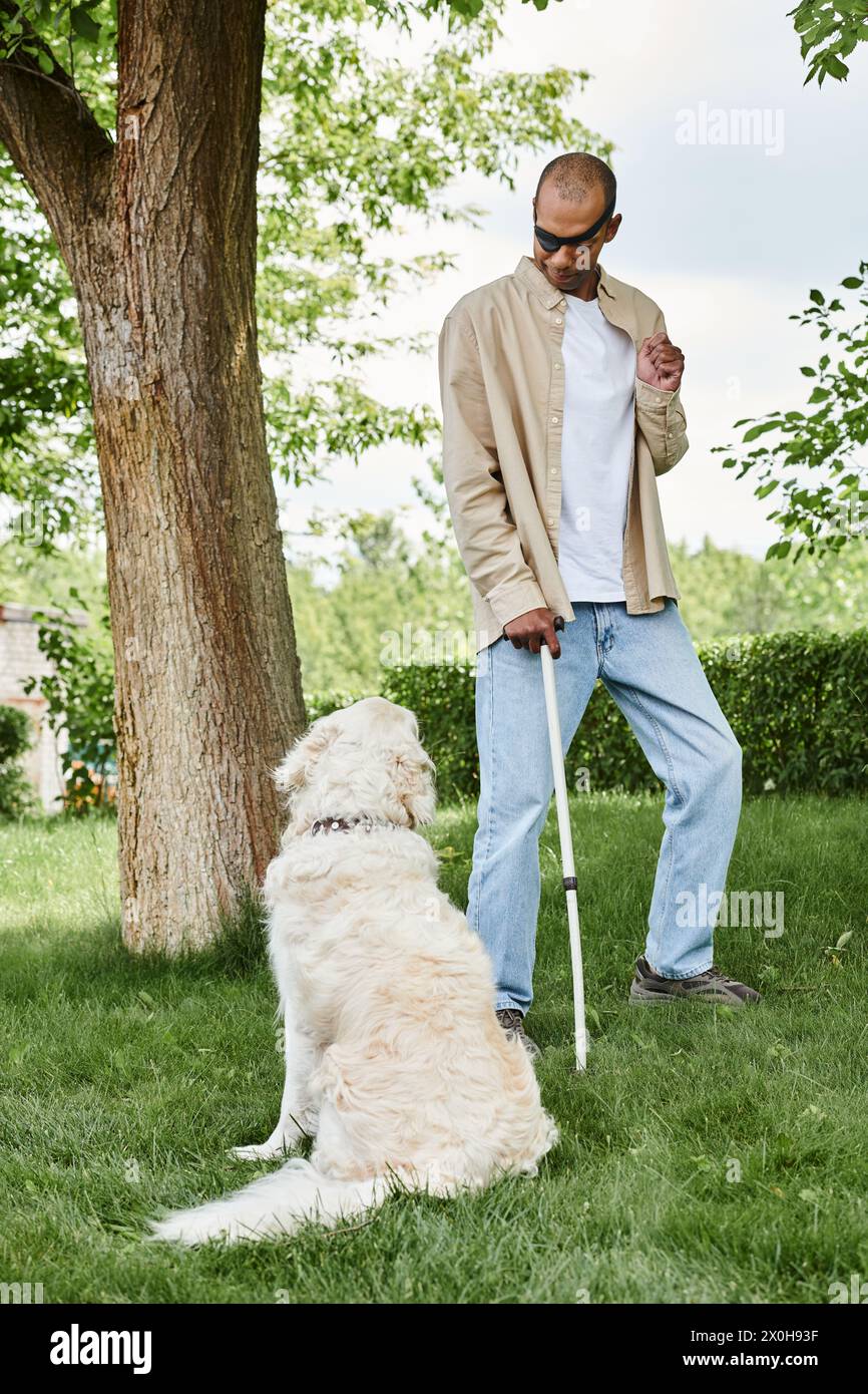 Un hombre afroamericano discapacitado con síndrome de miastenia gravis de pie junto a un perro labrador en un campo verde vibrante. Foto de stock