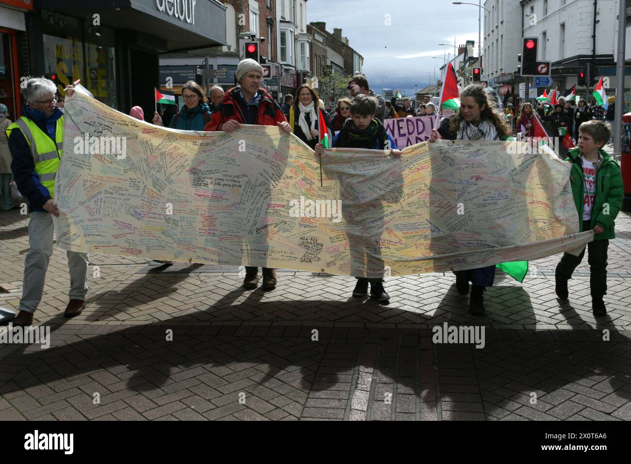 Rhyl, Reino Unido. 13 de abril de 2024. Los manifestantes llevan una pancarta con los nombres de todos los civiles palestinos conocidos muertos durante la manifestación. Más de 150 partidarios pro-palestinos de todo Gales llevaron la protesta a las calles para exigir el cese del fuego en Gaza y detener el genocidio. Crédito: SOPA Images Limited/Alamy Live News Foto de stock