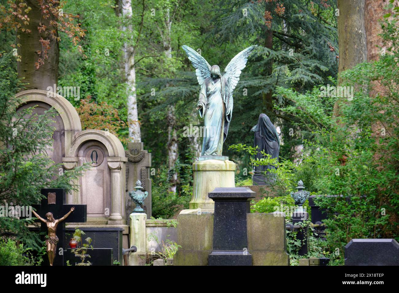 un ángel en un pedestal en medio de tumbas históricas en el entorno boscoso del cementerio melaten de colonia Foto de stock