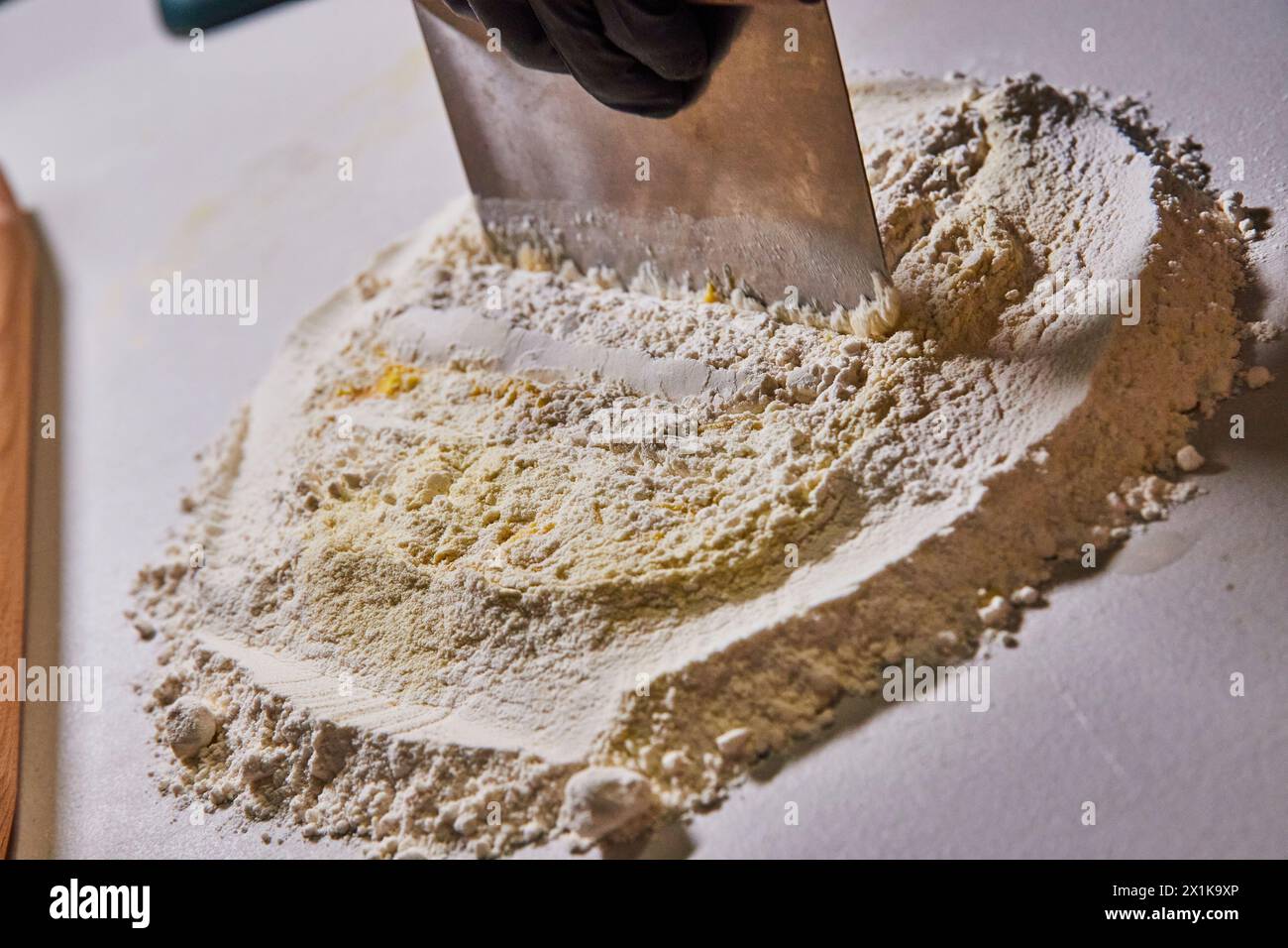 Preparación para hornear con harina y raspador de banco, detalle de mano con guantes Foto de stock