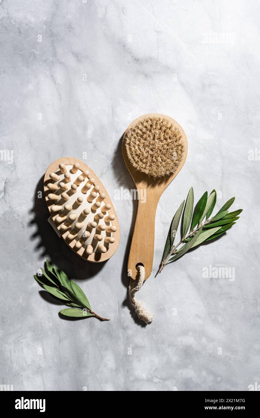 Cepillo de bambú de madera para el masaje seco y hojas verdes de eucalipto sobre fondo de mármol. Spa en casa, cuidado natural del cuerpo y concepto de relajación. Foto de stock