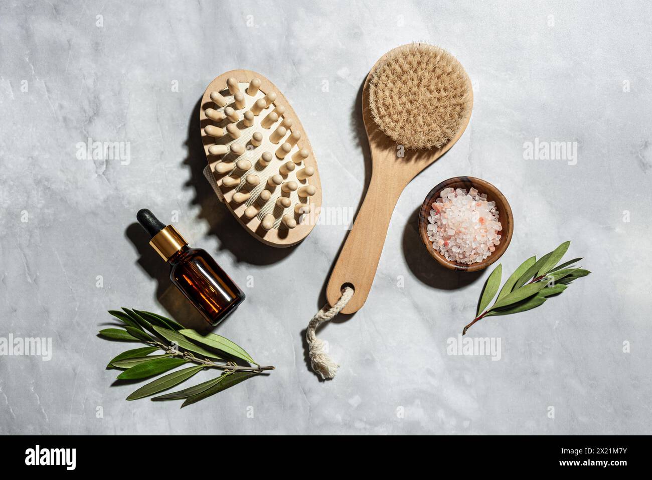 Cepillo de bambú de madera para el masaje seco, sal marina, aceite y hojas verdes de eucalipto sobre fondo de mármol. Home SPA, drenaje linfático, eco cuerpo natural ca Foto de stock