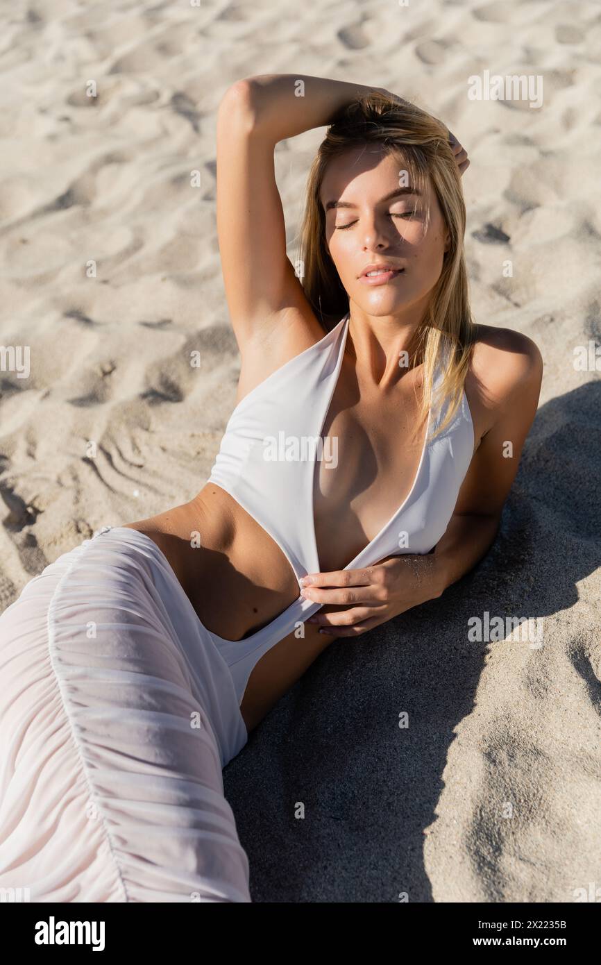 Una joven rubia en bikini blanco se relaja en la orilla arenosa de Miami  Beach Fotografía de stock - Alamy