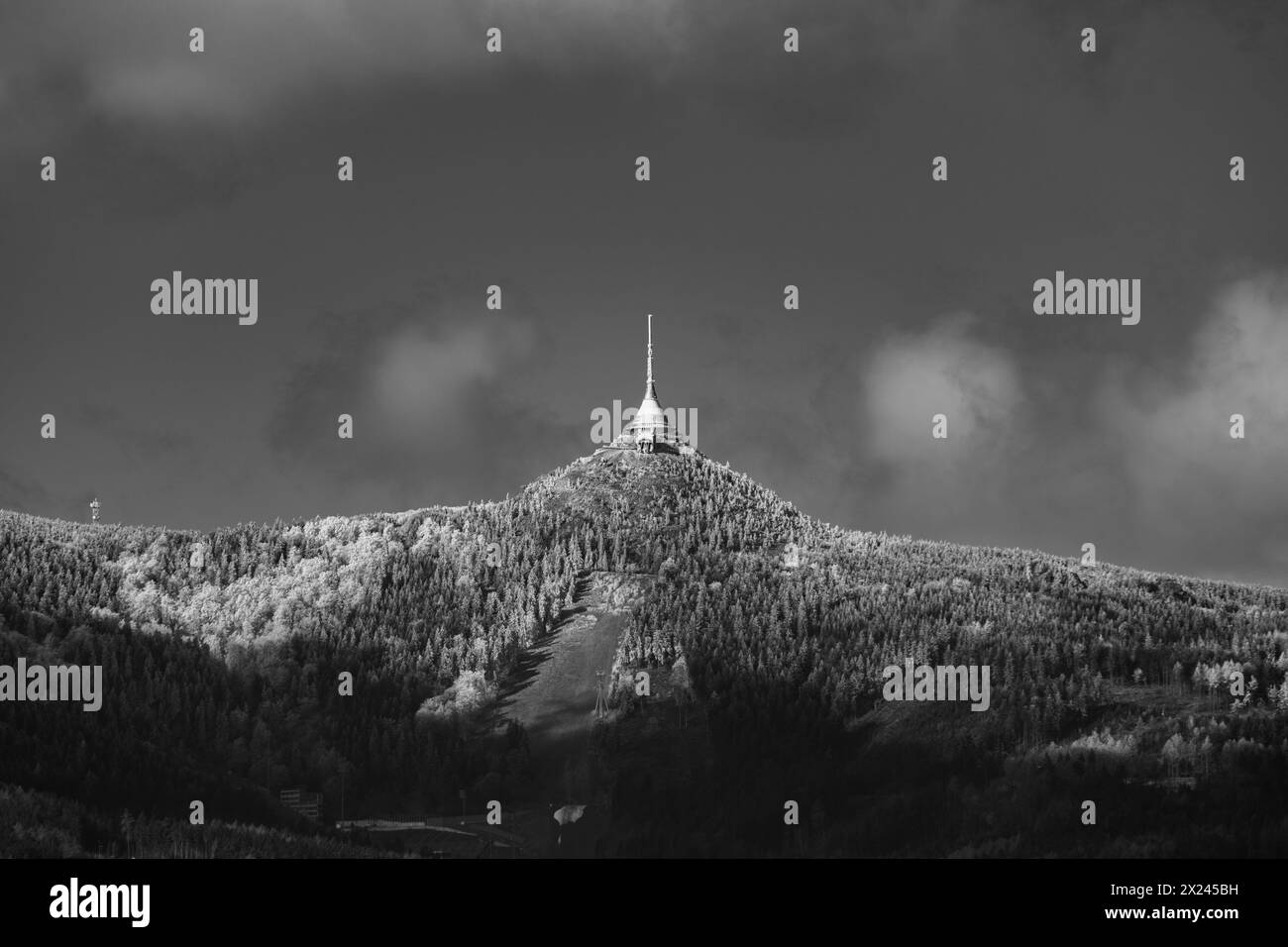 Una nítida vista matutina del pico Jested cubierto de nieve con su icónica torre de pie alto contra un cielo azul. Liberec, Chequia. Imagen en blanco y negro. Foto de stock