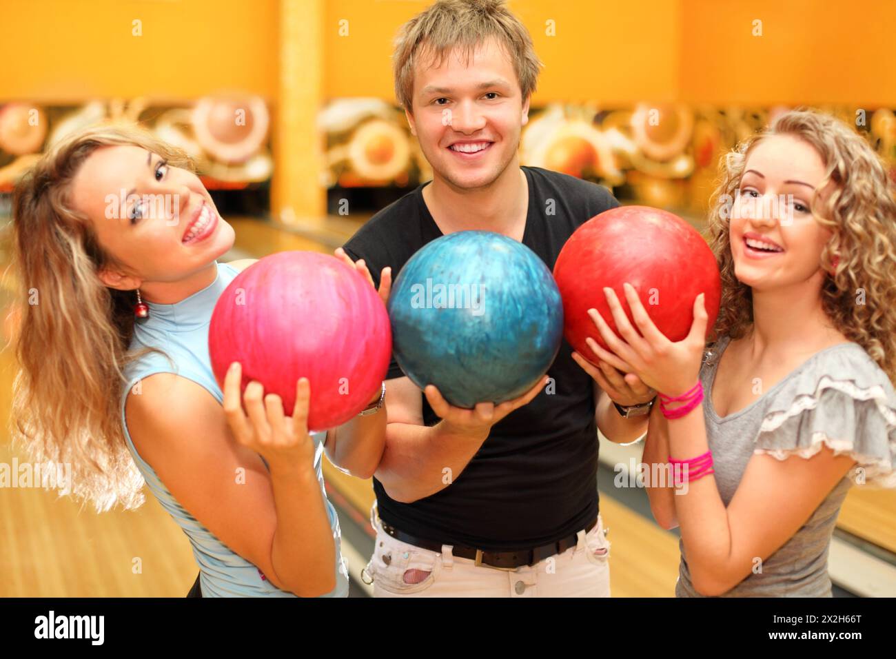 El hombre joven y dos hermosas chicas felices hicieron fila de bolas en el  club de bolos; se centran en el hombre Fotografía de stock - Alamy