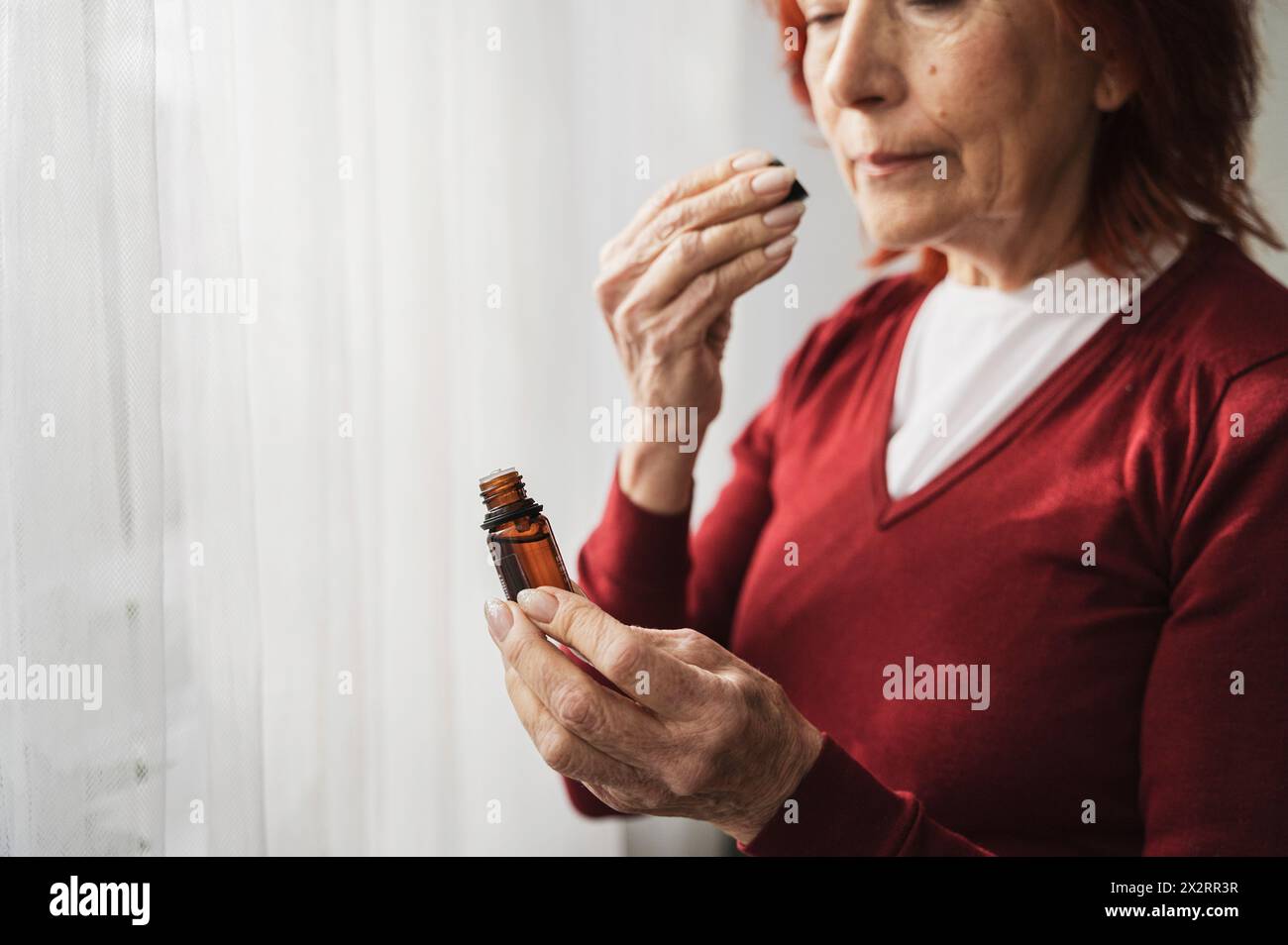 Mujer mayor que huele aceite esencial de la botella en casa Foto de stock