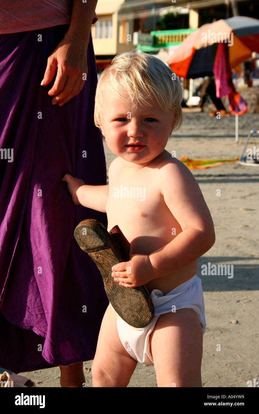 Hijo de pie en una playa con el apoyo de la madre y la celebración de una zapatilla en un lado Foto de stock