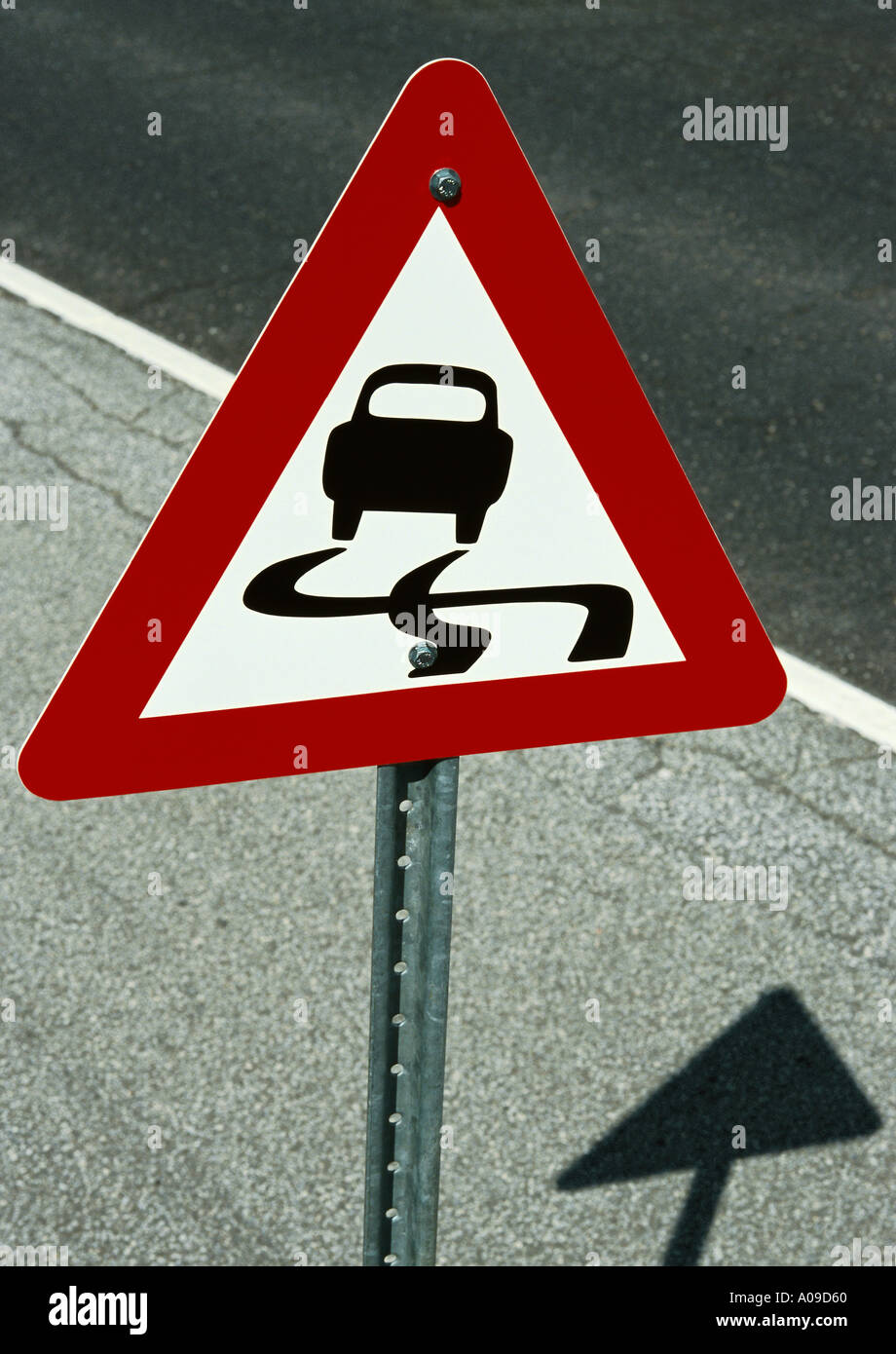 Un rojo blanco y negro resbalosa triangular firmar en un poste de metal situada sobre el hombro de una carretera pavimentada Foto de stock