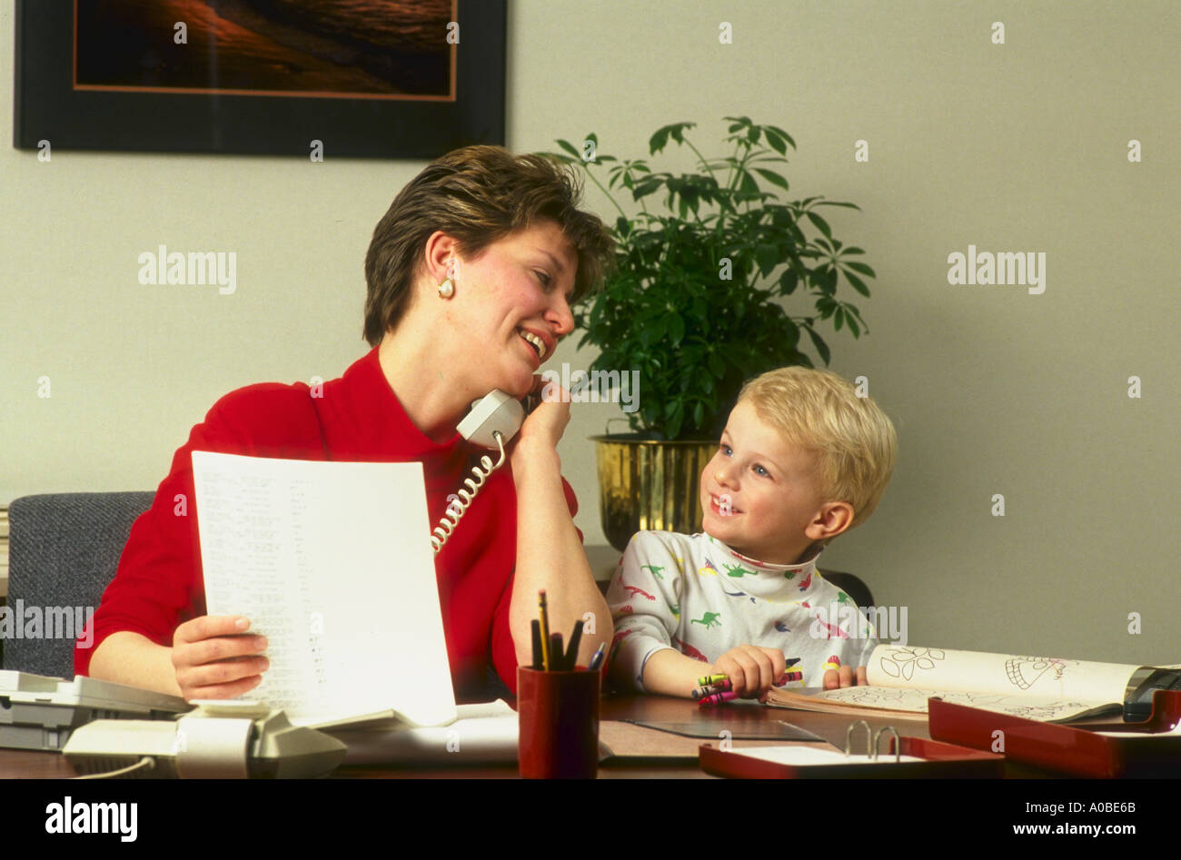 Working Mother en Office juggling tanto hablar por teléfono y respondiendo a su hijo al mismo tiempo Foto de stock